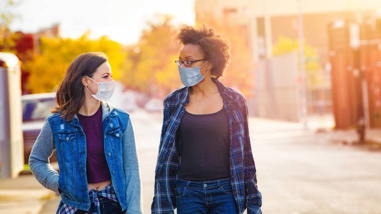 two friends having a discussion while walking and wearing masks