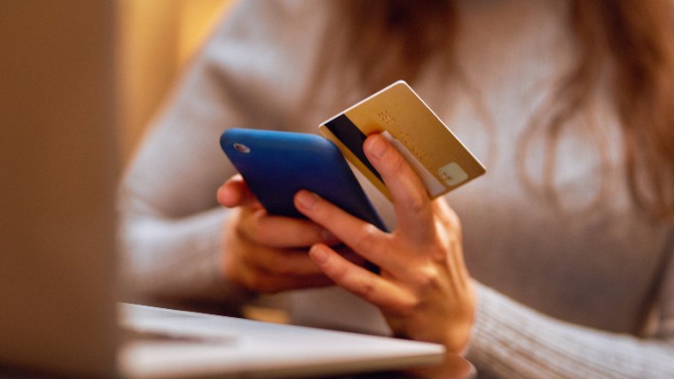 Woman holding cellphone and credit card, making a transaction.