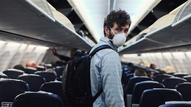 Man wearing a mask preparing to get off of an airplane.