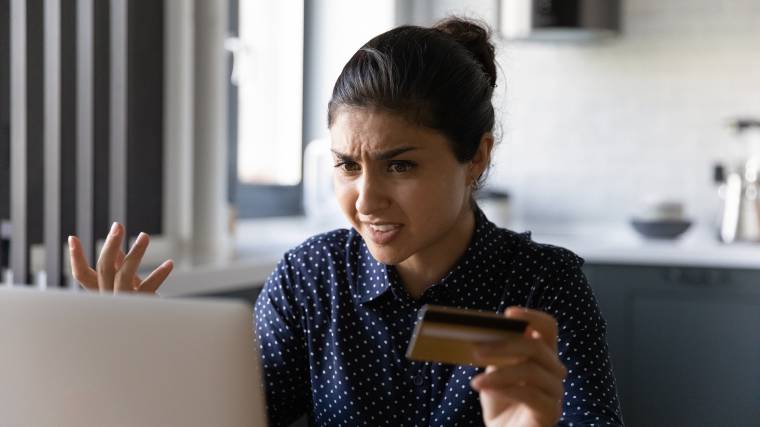Agitated woman holding a credit card while using a laptop.