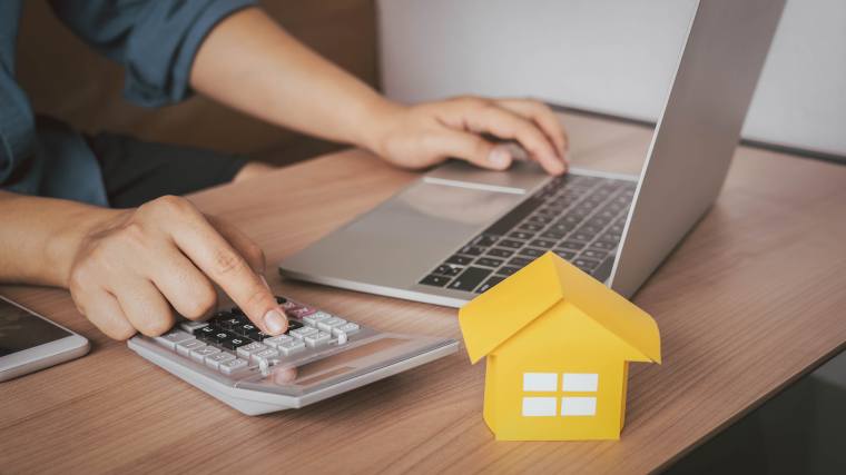 Model house on a desk with a laptop and calculator.