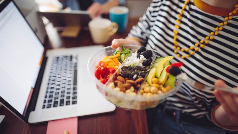 Sitting in front of a laptop, eating a takeaway salad.