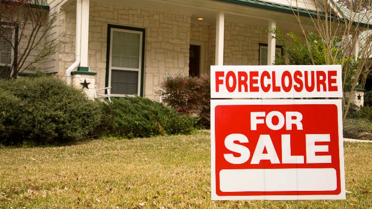 A "for sale" sign in front of a suburban house.