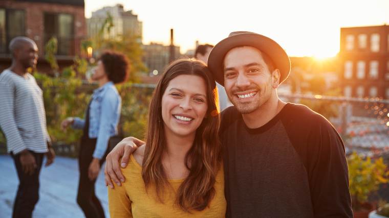 Young couple standing together at a rooftop party at sunset.