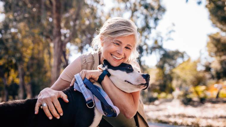 A woman in her fifties hugging her dog in a park.