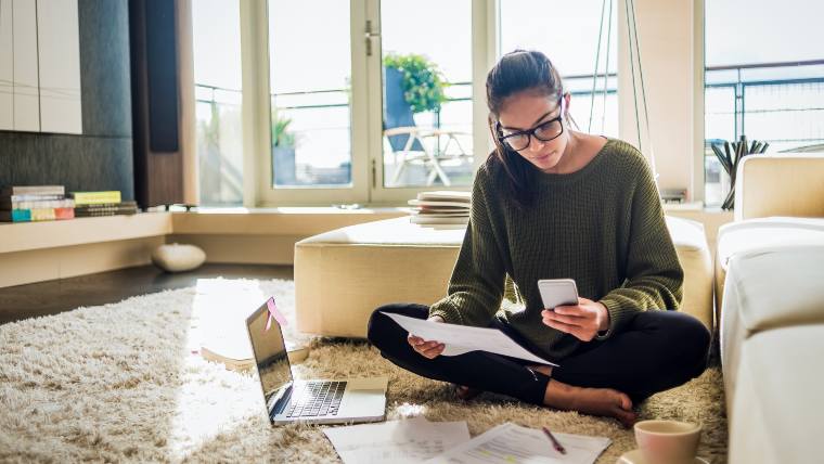 Woman reviewing documents, making a phone call, and using a laptop in her living room.