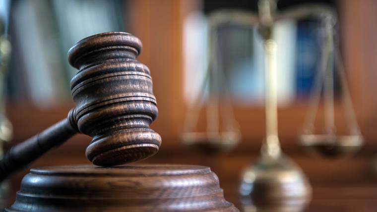 A gavel in the foreground and the scales of justice in the background.