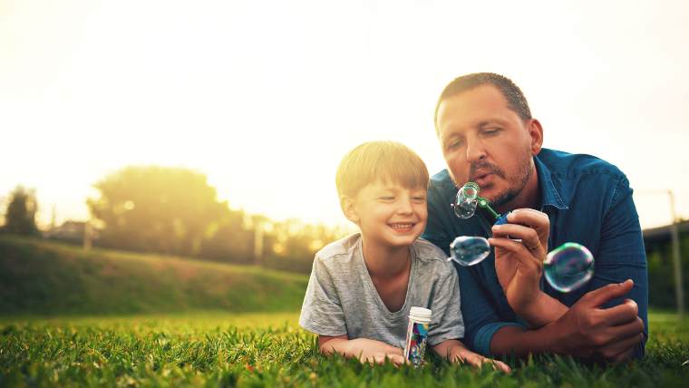 Father and son blowing bubbles together in a field.