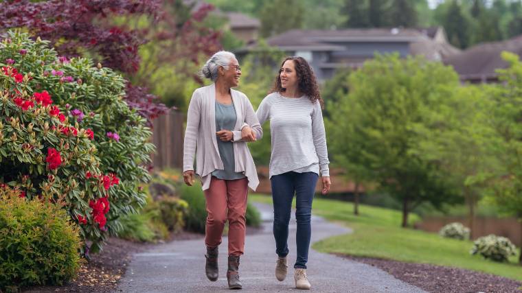 Adult daughter and her senior mother walk and talk together.