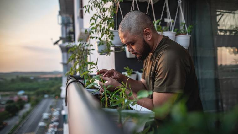 Man tending his plants on the balcony of his apartment.
