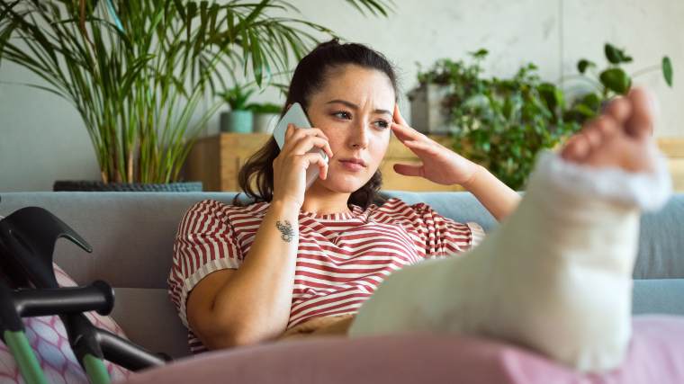 Young woman with her leg in a cast, making a phone call.