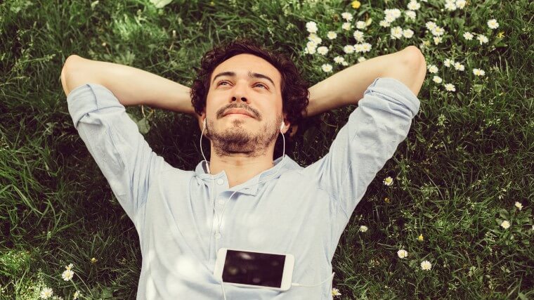 man relaxing in a field listening to music