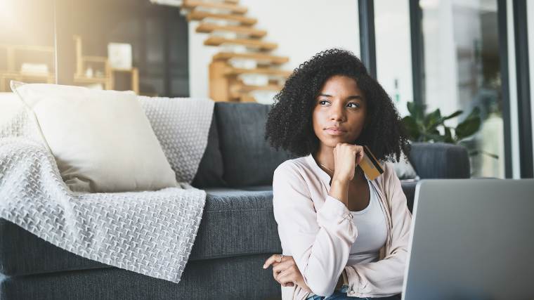 Woman sitting at laptop with credit card contemplating spending money