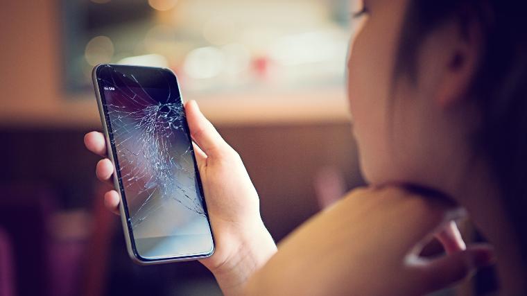 Woman looking at cracked smartphone.