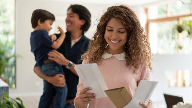 woman opening mailing with husband and small child in the background