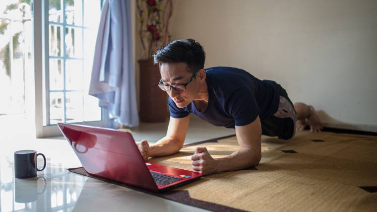man exercising at home and using a laptop
