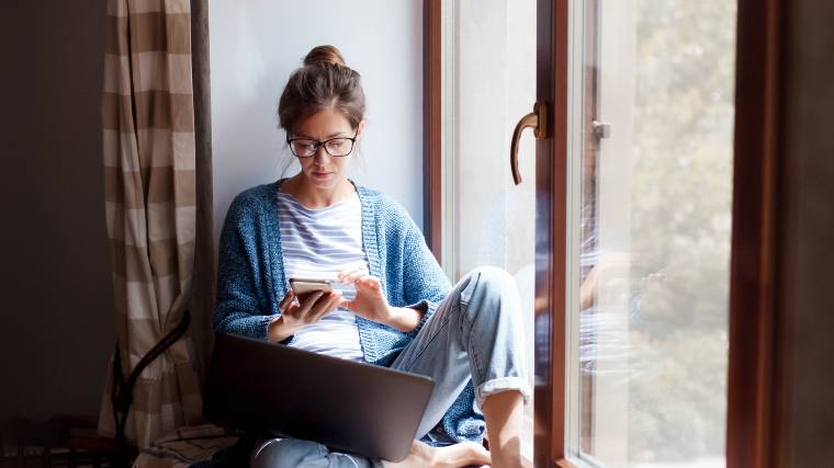 woman checking her phone while using her laptop