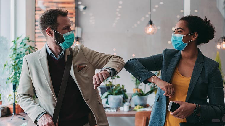 A man and woman wearing masks joyfully bump elbows during a pandemic.