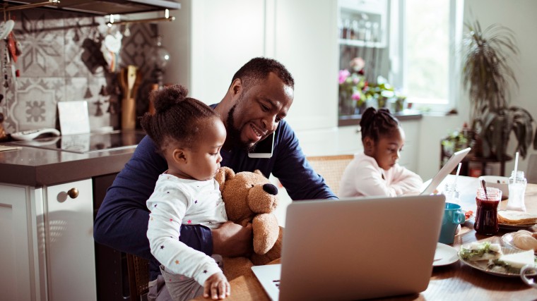 Young father working at the table while watching two young daughters.