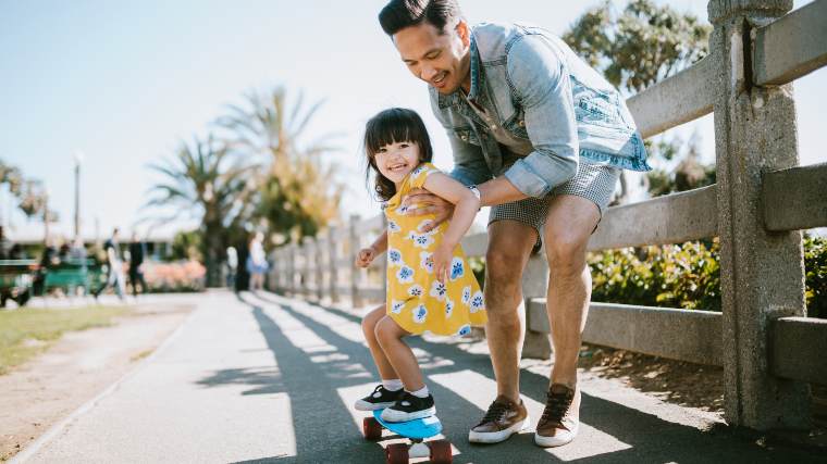 A father teaching his young daughter how to skateboard.