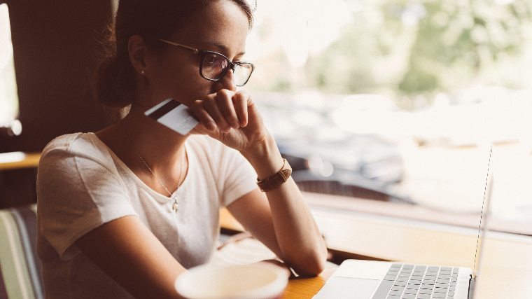 Woman using laptop and holding credit card.