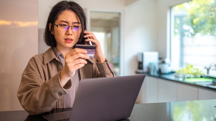 Woman looking at credit card while on the phone.