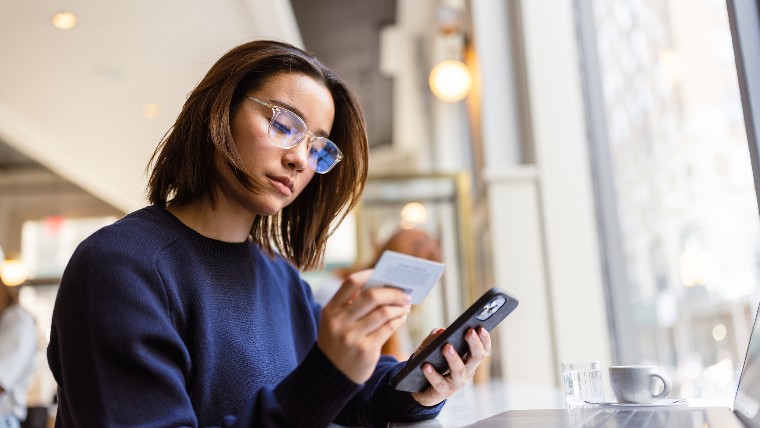 Young woman entering credit card info into cellphone.