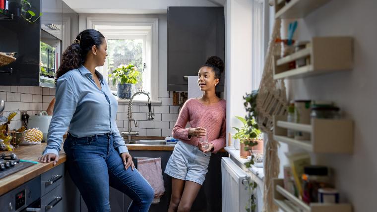 Mother and teenaged daughter talking in kitchen.