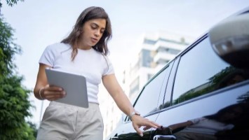 Woman holding clipboard inspecting car.