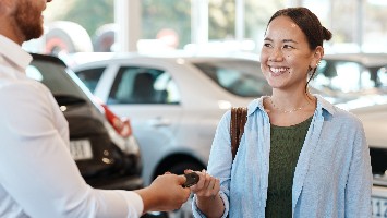 Young woman receiving keys to new car.
