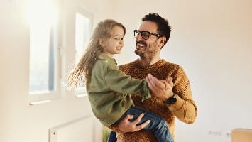 Father holds young daughter in his arms.