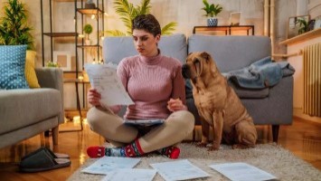 Woman sits on floor with her dog while completing her taxes.