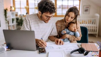 Young couple with baby sitting at table reviewing finances.
