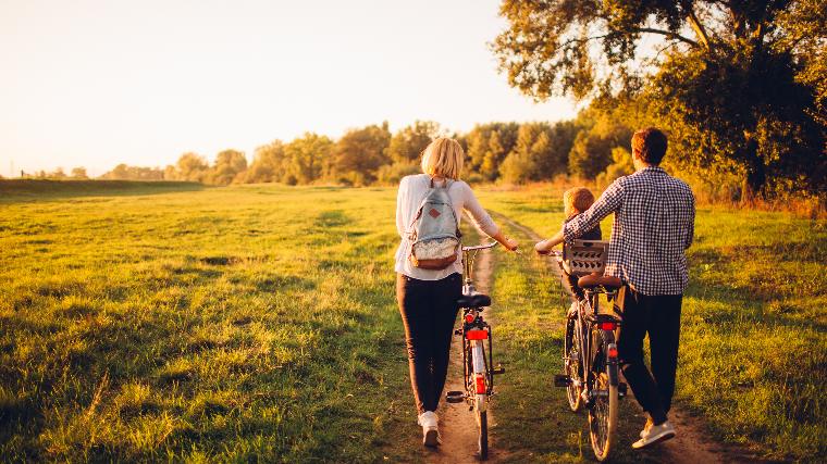 Young parents with small child walking in nature with bikes.