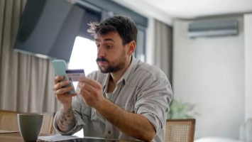 Overwhelmed man holding up phone and credit card.