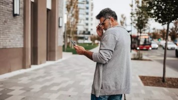 Man on street looks at phone.