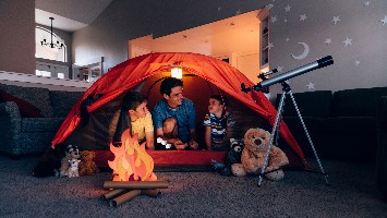 Father and two young sons camping in living room.