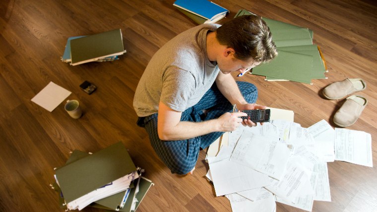 Man sitting on floor surrounded by documents.