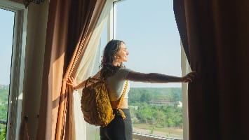 Young woman looks through window at vacation resort.