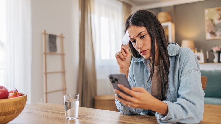 Stressed young woman holding credit card and looking at phone.