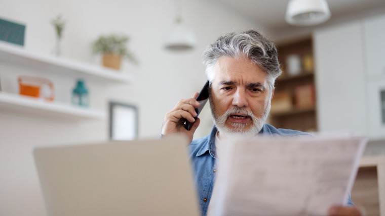Worried man on phone while reading bills.