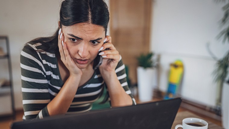 Young woman looking stressed while talking on the phone.