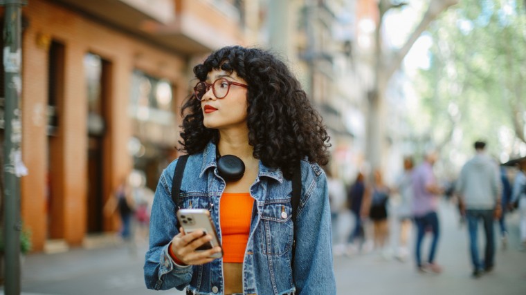 Young woman holding phone while walking in city.
