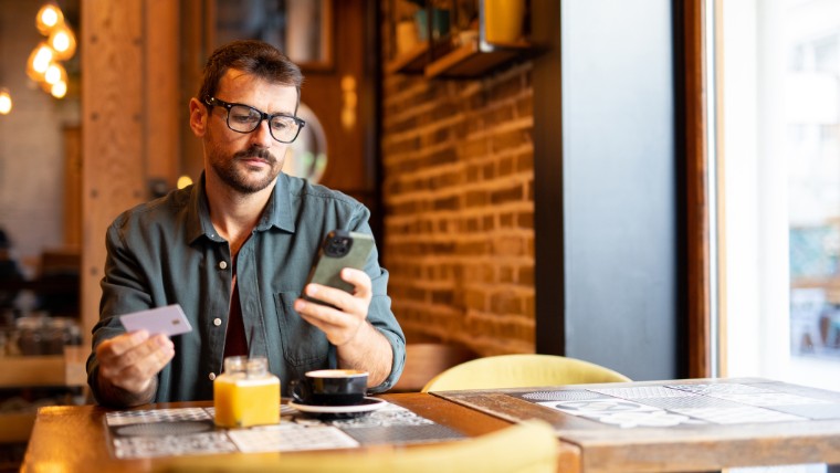 Man at cafe holding credit card and looking at phone.