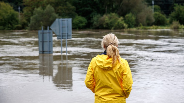 Woman in rain jacket looking at flood water.