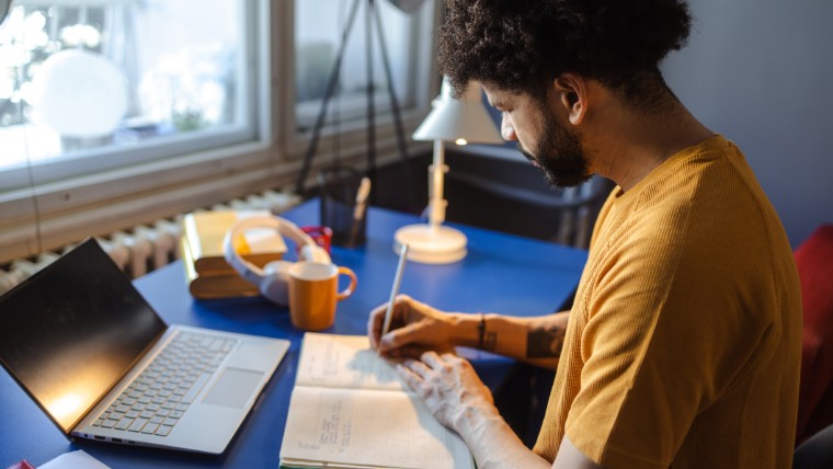 Man taking notes while using a laptop.