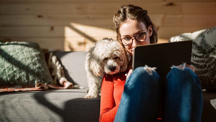 Woman looking at tablet while her dog peers over her shoulder.